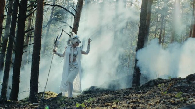 Female model dressed like a satyr is posing in a forest. She is representing mythological evil character, moving hands in background of fume