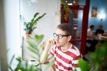 Contemporary businessman talking by mobile phone while sitting in front of window in cafe