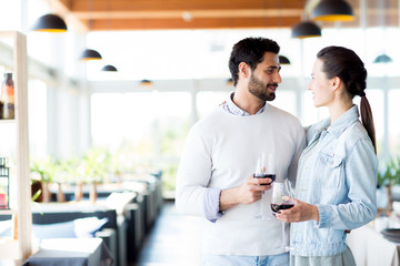 Young amorous and affectionate couple with glasses of red wine looking at one another in restaurant