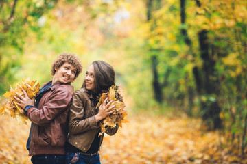 Loving happy couple in autumn in park holding autumn maple leaves in hands.