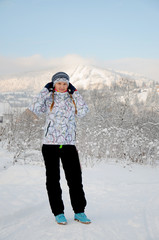 Fototapeta na wymiar Happy woman on snow in Carpathian mountains. On background of forest and ski slopes. Close up. Winter nature. Portrait of a girl standing. Heavy snow falls.