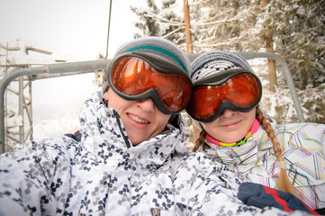Happy man and woman in ski eyeglasses rises on the lift in Carpathian mountains. On background of forest and ski slopes. Close up. Winter nature.