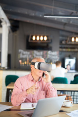Fototapeta na wymiar Modern and mobile businessman in vr headset talking to clients by smartphone and networking in cafe