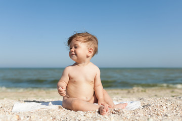 Fototapeta na wymiar little child sitting on a towel by the sea naked cheerful and happy