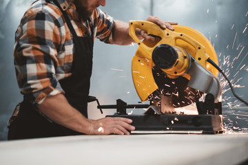 Bearded worker mechanic using electrical angular grinding machine in metalworking plant. Work in...