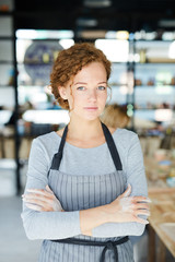 Young potter in apron crossing her arms on chest while spending day in workshop