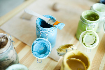 Open jars with gouache of various colors on workplace of modern craftsperson