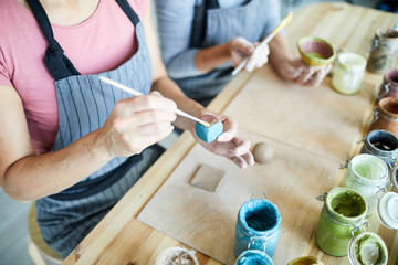 Female master of clay craft painting self-made dice in blue color over workplace