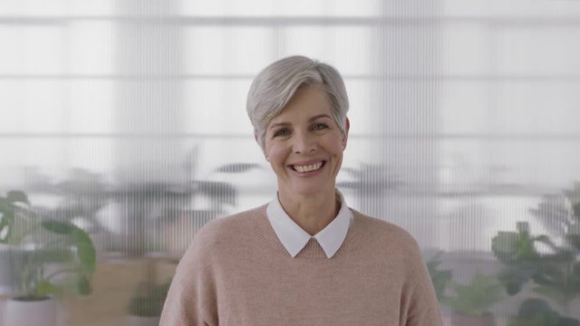 portrait of elegant mature business woman smiling looking at camera enjoying successful lifestyle senior female wearing jersey in office workspace background