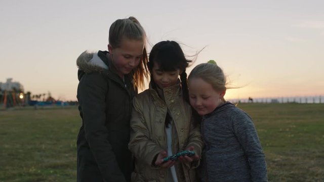 portrait of little girls posing taking selfie photo using smartphone camera technology enjoying park outdoors at sunset