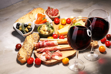 Italian antipasti wine snacks set. Cheese variety, Mediterranean olives, crudo, Prosciutto di Parma, salami and wine in glasses over stone grunge background.