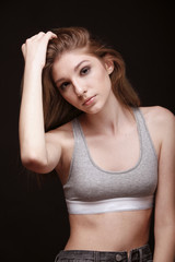 one person, teenage girl posing, looking to camera, upper body shot. wearing top and jeans. hand moving touching hair. looking to camera, studio shot, black background. front view.