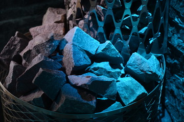 A stove in the sauna with stones with blue illumination.