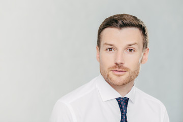 Attractive male freelancer with confident serious expression, works distantly, dressed in elegant white shirt with tie, isolated over white studio wall. People, facial expressions and work concept