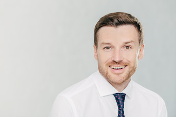 Studio shot of handsome unshaven male entrepreneur with cheerful expression, rejoices raising sales, dressed in formal clothes, isolated over white background with copy space aside for your text