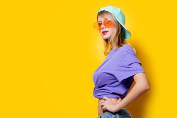 Young style girl with orange glasses and cap on yellow background. Clothes in 1980s style