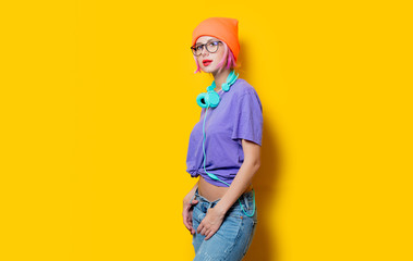 Young style girl in purple clothes with headphones on yellow background.  Clothes in 1980s style