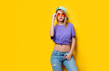 Young style girl with orange glasses and cap on yellow background. Clothes in 1980s style