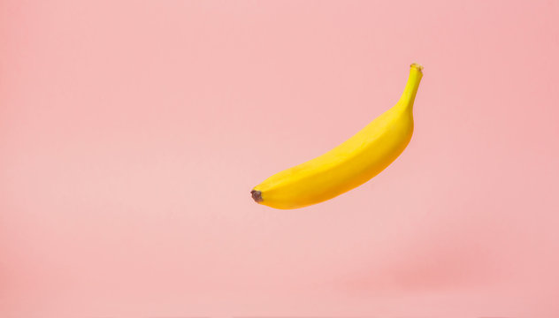 One yellow banana levitate in air on pink background.
