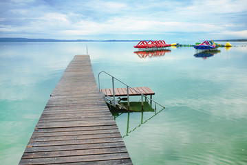 Tranquil scene of Lake Balaton with a pier and pedal boats in the background.