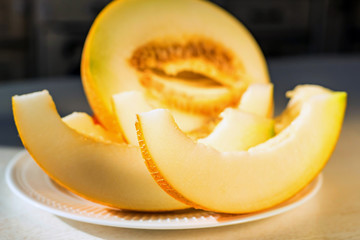 Half melon and melon slices on white plate close