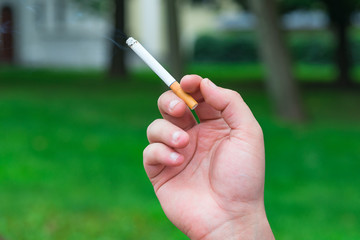 Cigarette in the hand with smoke on a green background