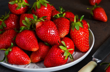 Fresh, juicy strawberries in a plate on a dark rustic background. Proper nutrition. Organic food.