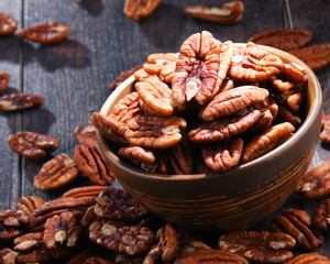 Bowl with pecan nuts on wooden table.