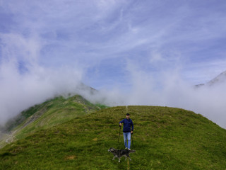 An active elderly man does walks in the mountains with his dog.