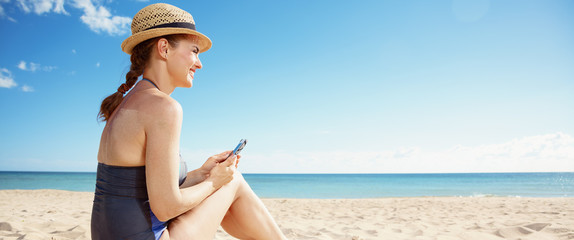 happy woman with smartphone looking into distance on seacoast