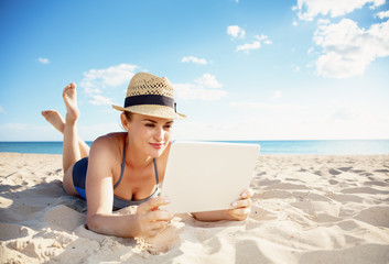 young woman in swimwear on beach using tablet PC