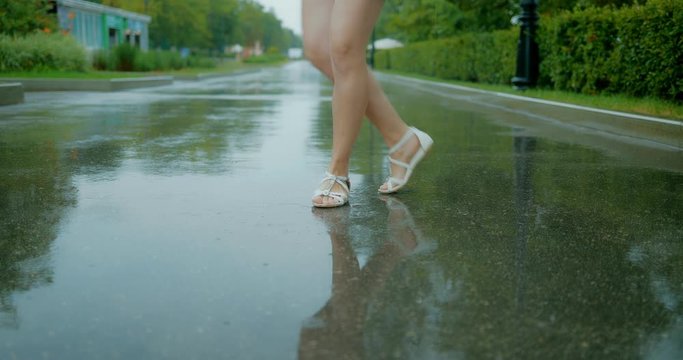 Close-up legs. Girl spinning in the rain on the wet asphalt
