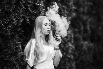 Vape teenager. A young cute white girl in a dress is vaping an electronic cigarette on the street in summer. Black and white.