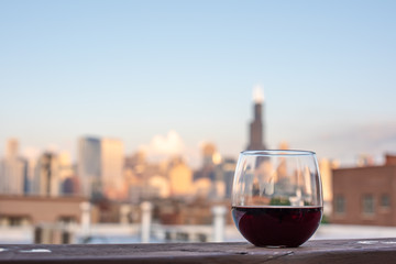Glass of red wine ready to be enjoyed on a rooftop with a beautiful cityscape blurred in the background.