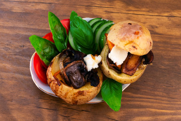 Baked potato tubers in the oven, stuffed with fried mushrooms with onions and carrots, decorated with slices of tomatoes, cucumbers and basil leaves.