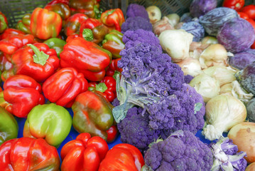 A rainbow of colorful red peppers, purple broccoli, and onions at the farmers market 