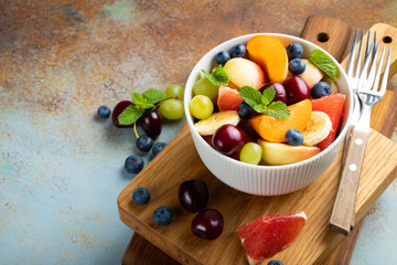 Bowl of healthy fresh fruit salad on a blue rusty background. Top view