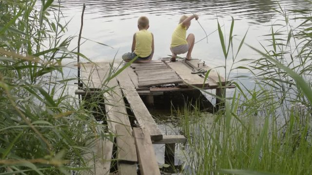 Happy children of village came to river to swim and fish. Boys are happy together on summer holidays in village. Reeds, wooden bridge, boat