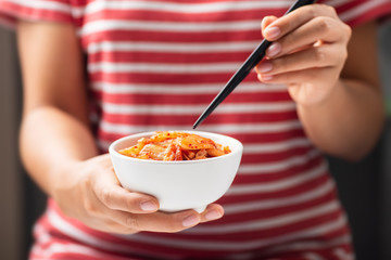 Woman holding chopsticks for eating kimchi cabbage in a bowl, Korean food