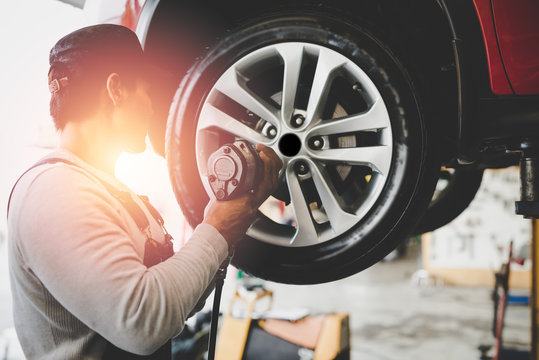 Asian young mechanic working holding the device changing tyre of car. Repair service..