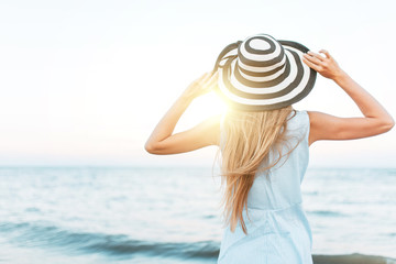 Girl looking into the distance, against the blue sea, summer mood, woman in hat