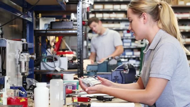 Engineer Helping Female Apprentice In Factory To Measure Component Using Micrometer