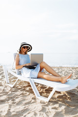 Freelancer girl working on vacation, in front of the beautiful sea, sitting with a laptop on the ocean