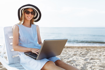 Beautiful girl sitting with a laptop on a chaise longue, a woman working on vacation, job search