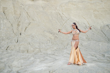 beautiful Caucasian woman belly dancer posing in desert with swords