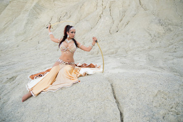 Young beautiful woman belly dancer posing in desert with swords