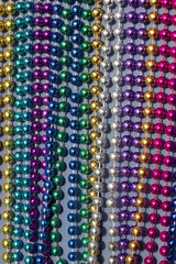 Multi-color Mardi Gras beads in rows on neutral blue background