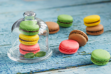 Green, pink and yellow french macarons under the glass on the wooden background