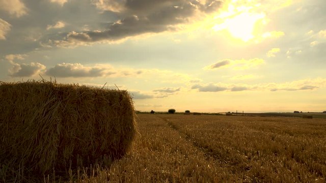 Pan shot of straw bale in field with country lane in background