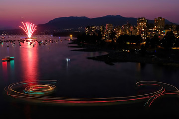 Fireworks in Vancouver. British Columbia. Festival of Lights in downtown Vancouver above the ocean against sunset sky and mountains. Colorful boat light treks on the water.  BC. Canada.